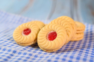 Çilek kremalı sandviç kurabiyeleri mavi ve beyaz bir kumaşa konur.
