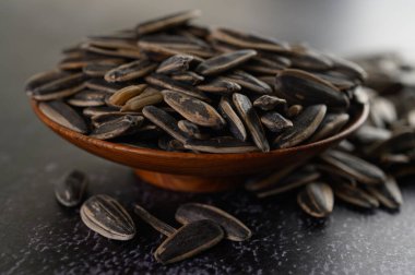 Siyah çimento zeminde, ahşap bir kasede güneş çiçeği tohumu..