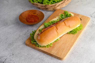 Tahta üzerinde domates soslu hotdog ve dokuma sepetinde marul, kopyalama alanı.