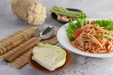 Beyaz tabakta Tayland papayası salatası, pilav, kaşık ve çatal..