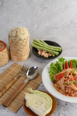 Beyaz tabakta Tayland papayası salatası, pilav, kaşık ve çatal..