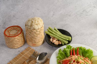 Beyaz tabakta Tayland papayası salatası, pilav, kaşık ve çatal..