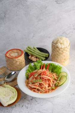 Beyaz tabakta Tayland papayası salatası, pilav, kaşık ve çatal..