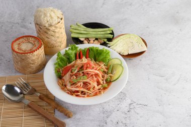 Beyaz tabakta Tayland papayası salatası, pilav, kaşık ve çatal..