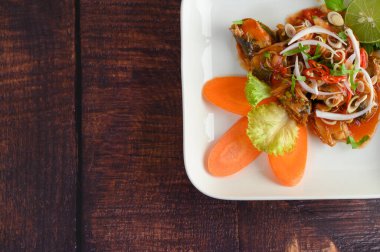 Baharatlı domates soslu sardalya salatası ve bitki karışımı, ahşap masada beyaz tabakta balık şeklinde güzelce düzenlenmiştir.