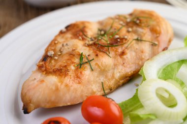 Beyaz tabakta ızgara tavuk, domates, salata ve soğanlı..