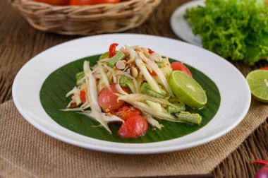 Tahta bir masada beyaz bir tabakta Papaya Salatası (Som tum Thai).