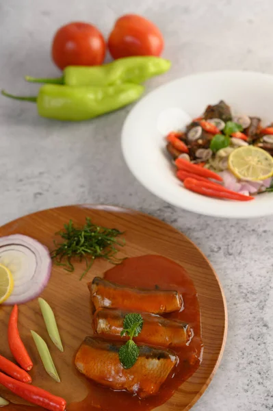 Vertical image, selective focus the sardine in tomato sauce on wooden tray, blurred spicy Canned Sardine Salad with herb ingredient in white dish, copy space