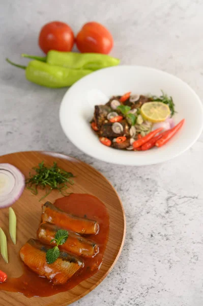 Vertical image, selective focus the sardine in tomato sauce on wooden tray, blurred spicy Canned Sardine Salad with herb ingredient in white dish, copy space