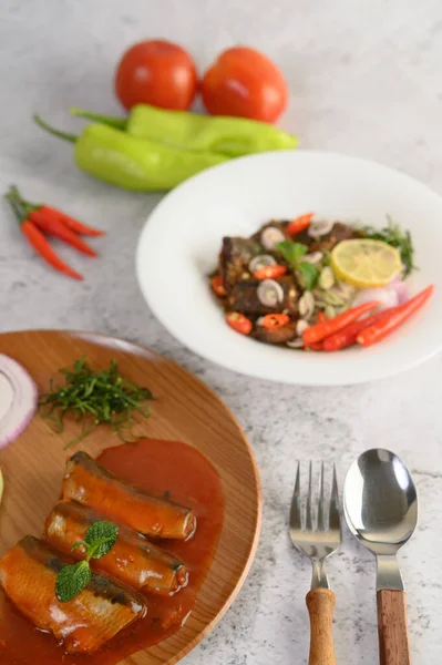 Vertical image, selective focus the sardine in tomato sauce on wooden tray, blurred spicy Canned Sardine Salad with herb ingredient in white dish, copy space