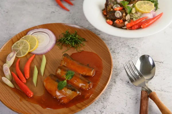 selective focus the sardine in tomato sauce on wooden tray, blurred spicy Canned Sardine Salad with herb ingredient in white dish, copy space