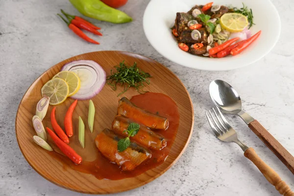 selective focus the sardine in tomato sauce on wooden tray, blurred spicy Canned Sardine Salad with herb ingredient in white dish, copy space