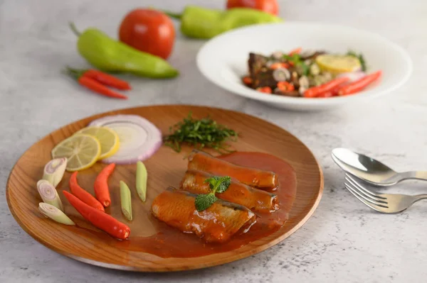 selective focus the sardine in tomato sauce on wooden tray, blurred spicy Canned Sardine Salad with herb ingredient in white dish, copy space