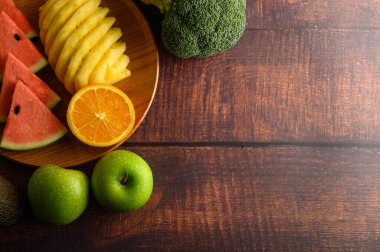 Karpuz, ananas, portakal, avokado, brokoli ve ahşap masada elmalarla parçalara ayrılmış. Üst görünüm.