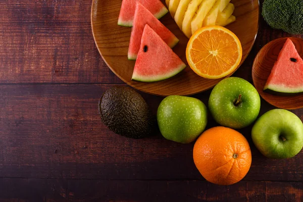 Watermelon, pineapple, oranges, cut into pieces with avocado, Broccoli and apples on wood table. Top view.