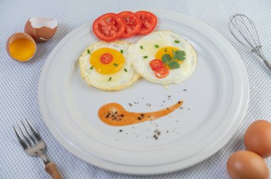 Dilimlenmiş taze soğan ve dilimlenmiş domatesle beyaz bir tabakta kızarmış yumurta.