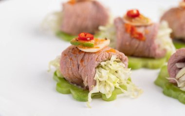 Acı kavun, galangal, biber, domates ve sarımsaklı baharatlı limon salatası siyah beton zeminde beyaz bir tabakta..