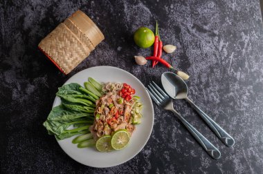 Siyah beton zeminde beyaz tabakta lahana, galangal, biber ve sarımsaklı baharatlı limon salatası..