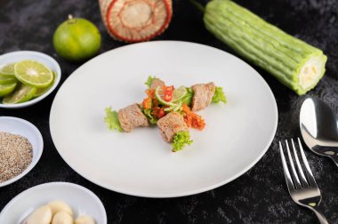 Acı kavun, galangal, biber, domates ve sarımsaklı baharatlı limon salatası siyah beton zeminde beyaz bir tabakta..