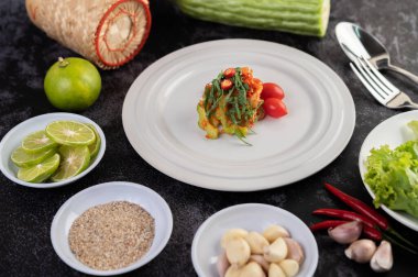 Acı kavun, galangal, biber, domates ve sarımsaklı baharatlı limon salatası siyah beton zeminde beyaz bir tabakta..