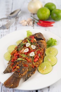 Acı biber soslu kızarmış tilapia, limon salatası ve beyaz ahşap bir masada bir tabakta sarımsak..
