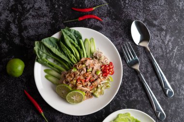 Siyah beton zeminde beyaz tabakta lahana, galangal, biber ve sarımsaklı baharatlı limon salatası..