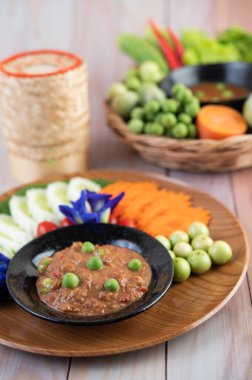 Patlıcan, havuç, biber ve ahşap sepetteki salatalıklarla dolu bir kasede acı biber ezmesi.