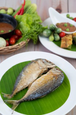 Kızarmış uskumru ahşap bir zeminde beyaz bir tabağa konur..