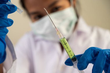 Maske ve eldiven takan bilim adamları kovid-19 'u önlemek için şırınga ve aşı tutuyorlar.