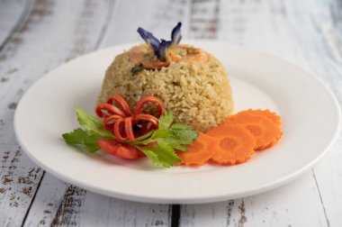 Domates ve havuçtan oluşan beyaz bir tabakta karidesli pilav..