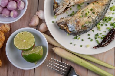 İki pişmiş uskumru, taze soğan serpiştirilmiş beyaz bir tabağa konur..