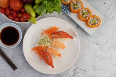 Suşi, yemek çubukları ve beyaz beton zemine batırılmış sos dolu bir tabakta..