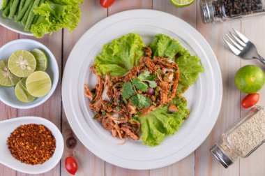 Salatalık, salatalık, marul ve ahşap masadaki garnitürle birlikte beyaz bir tabakta baharatlı tavuk..