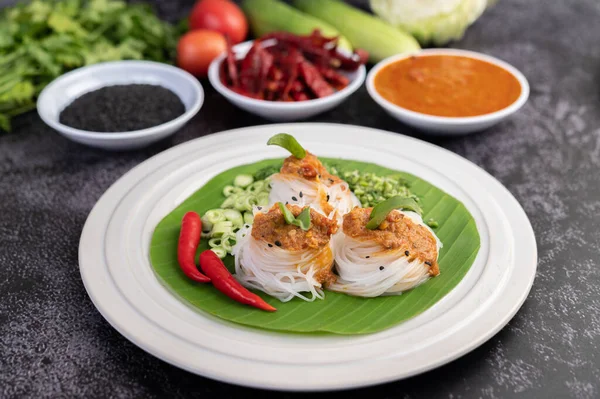 Noodles topped with coconut milk and vegetables and side dishes.