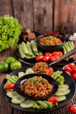 İçinde salatalık, uzun fasulye, domates ve meze olan siyah bir kasede tatlı domuz eti. Seçici odak.