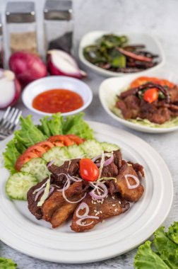 Susamlı kızarmış domuz eti, domatesler, salatalıklar, lahana ve beyaz bir tabağa konmuş marul..