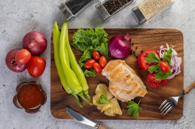 Biber, domates, kırmızı soğan, ananas sosu, marul ve susam tohumlarıyla ahşap tepsiye yerleştirilmiş tavuk bifteği.