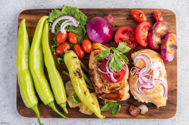 Biber, domates, kırmızı soğan, ananas sosu, marul ve susam tohumlarıyla ahşap tepsiye yerleştirilmiş tavuk bifteği.