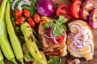 Biber, domates, kırmızı soğan, ananas sosu, marul ve susam tohumlarıyla ahşap tepsiye yerleştirilmiş tavuk bifteği.