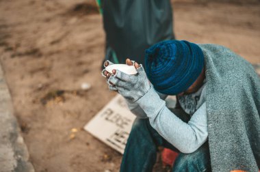 Adam elinde bir kupa ve parayla dilenci gibi oturuyor. Seçici odak.