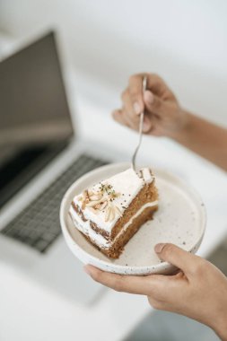 Kız pasta yiyor ve masada bir dizüstü bilgisayarı var. Seçici odak.