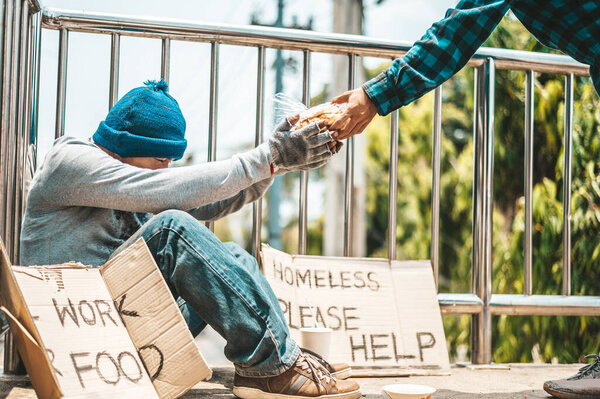The man sitting begging on an overpass with messages homeless people please help and work well with food.