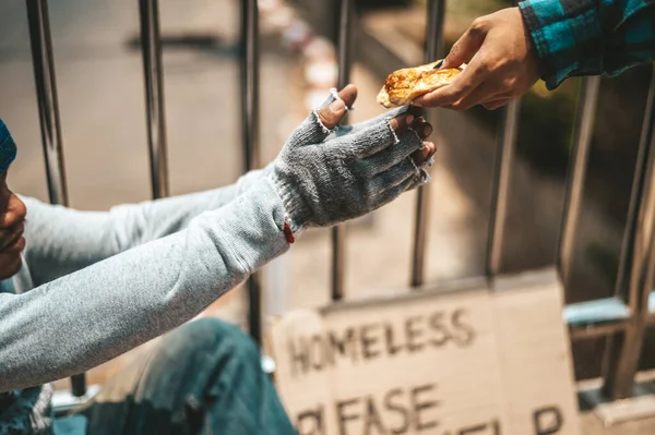 The man sitting begging on an overpass with messages homeless people please help and work well with food.