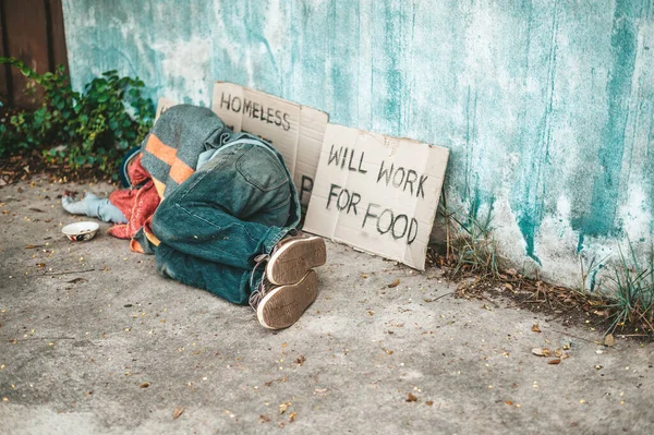 The beggars lay on their side of the street with dirty clothes.