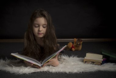 Karanlık bir odada kitap okuyan küçük kız.