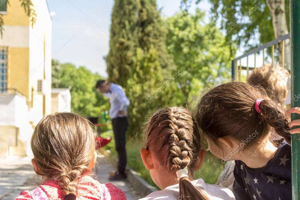 Small girls are watching a performance of a magician through an outdoor birthday party .