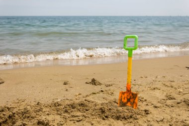 Sahildeki kumsalda sarı plastik oyuncak kürek. Metin için boş alan. Tatil, tatil konsepti.