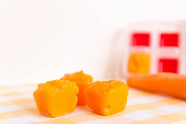 Готовлю детское питание, домашнее. Замороженная морковь, сделанная как кубик льда на жёлтой доске. Концепция здорового питания детей. Селективный фокус . — стоковое фото