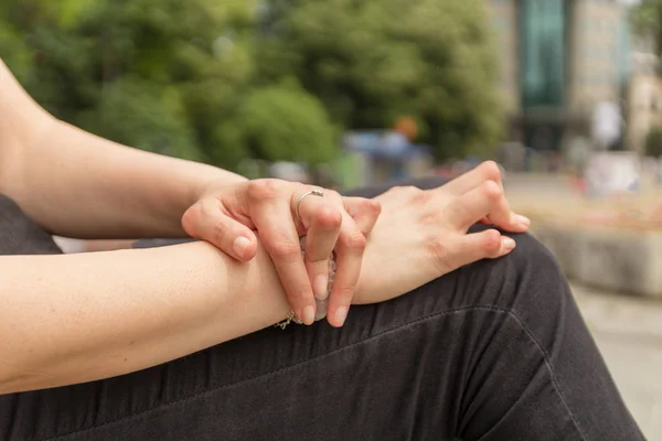 Una mujer joven con artritis reumatoide descansa sentada en un banco en un patio de un hospital. Las manos y las piernas están deformadas. Siente dolor. Enfoque seleccionado . — Foto de Stock