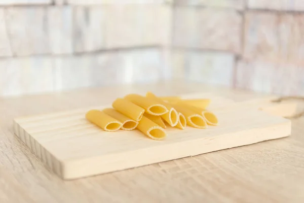 Raw, uncooked pasta. Macaroni on wooden cutting board on table at the kitchen. Selective focus — Stock Photo, Image